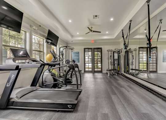 A spacious home gym with a treadmill, exercise bike, and suspension trainer.