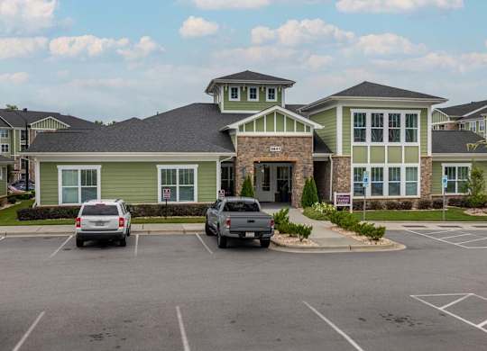 A parking lot in front of a building with a green and grey exterior at Foxwood Apartments, North Carolina, 27616