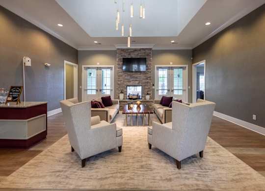 Two white chairs are placed on a rug in a room with a stone fireplace at Foxwood Apartments, Raleigh-Durham, North Carolina