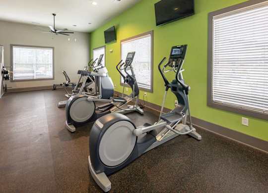 A gym with exercise bikes and a television on the wall at Foxwood Apartments, North Carolina, 27616