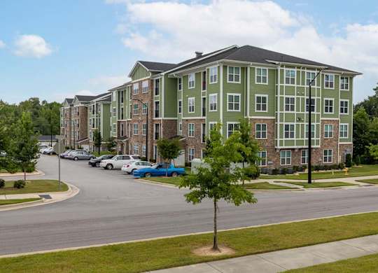 A tree stands in front of a green building at Foxwood Apartments, North Carolina