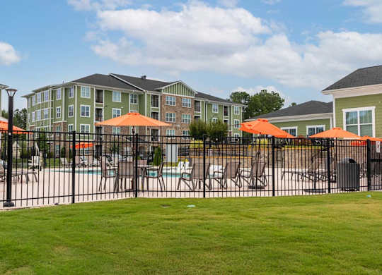 A black fence surrounds a pool area with orange umbrellas at Foxwood Apartments, Raleigh-Durham, NC, 27616