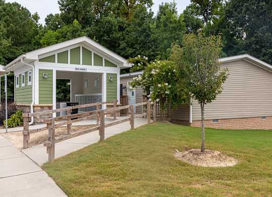 A green and white building with a porch and a tree in front of a beige building at Foxwood Apartments, Raleigh-Durham, North Carolina