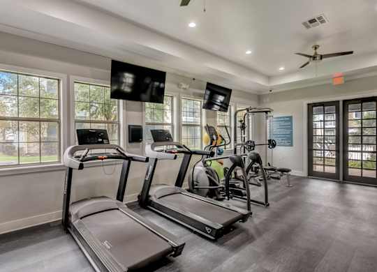 A spacious gym with treadmills, elliptical machines, and a fan.