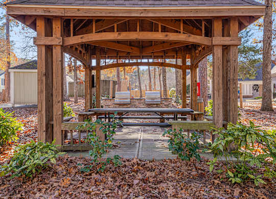 A wooden gazebo with a roof and a bench in front of it.
