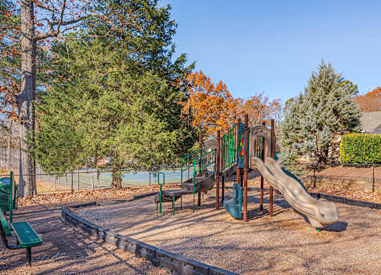 A playground with a slide, swings, and a green bench.