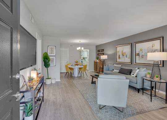 A well-lit living room with a grey sofa and a dining table set for four.