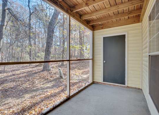 A screened porch with a sliding door leading to a wooded area.