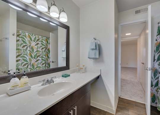 A bathroom with a floral shower curtain and a mirror above a double sink.