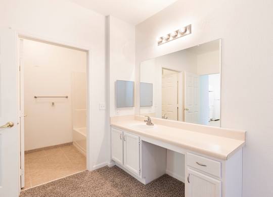 A white bathroom with a vanity and a mirror.
