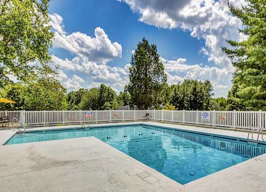 A large outdoor swimming pool surrounded by a white fence and trees. at Brandemere Apartment Homes, North Carolina, 27106