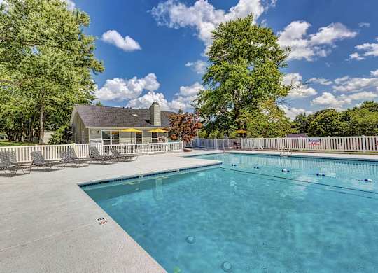 A large swimming pool surrounded by trees and a house in the background. at Brandemere Apartment Homes, North Carolina