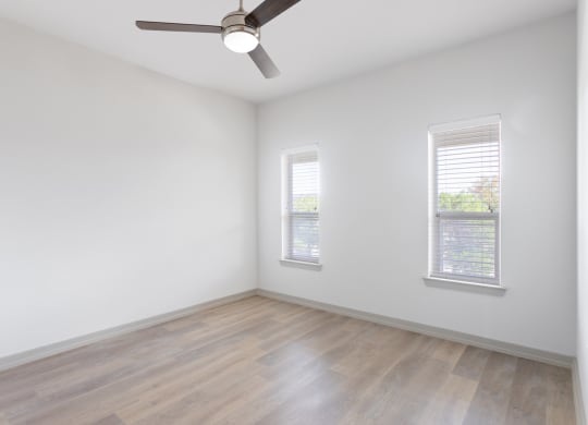 an empty room with a ceiling fan and two windows