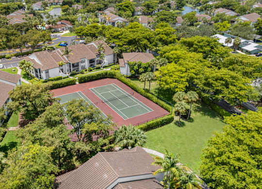 A tennis court is surrounded by apartments and trees.