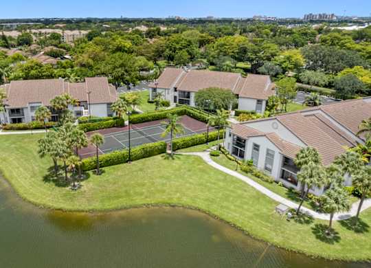 A bird's eye view of a residential area with apartments, a pond, and a sports court.