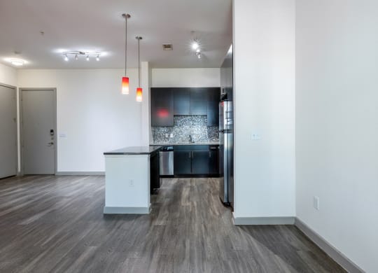 the living room and kitchen of an apartment with white walls and wood flooring