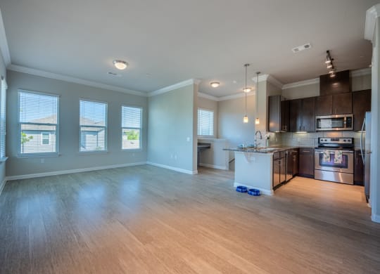 Living room with hardwood flooring facing kitchen with stainless steel appliances