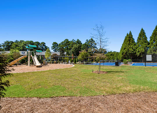 a playground with a swing set and a tennis court in the background at Caveness Farms Apartments, North Carolina 