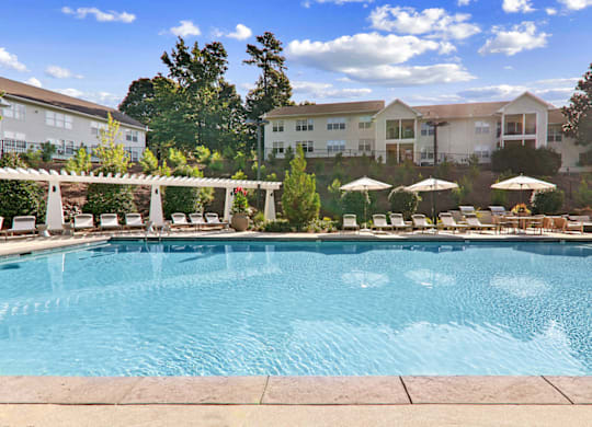 a swimming pool with lounge chairs and umbrellas in front of a building at Caveness Farms Apartments, Wake Forest 