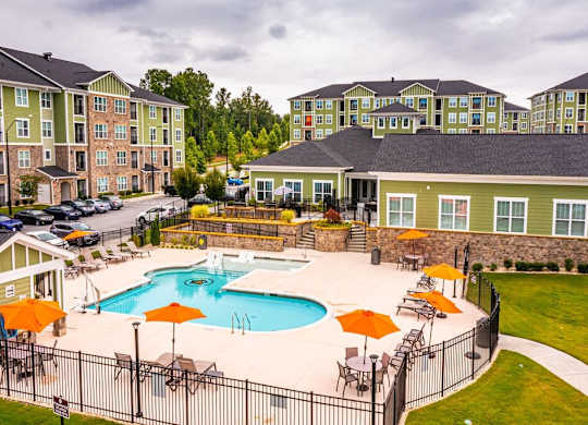 A pool surrounded by a black fence and orange umbrellas at Foxwood Apartments, Raleigh-Durham, 27616
