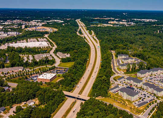 A highway curves through a wooded area with apartment buildings on one side and a parking lot on the other at Foxwood Apartments, North Carolina