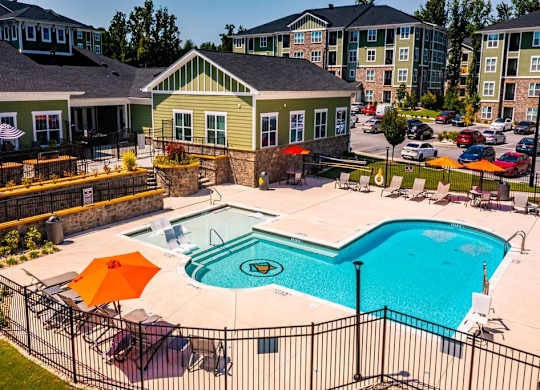 A pool surrounded by a black fence with orange umbrellas at Foxwood Apartments, North Carolina, 27616