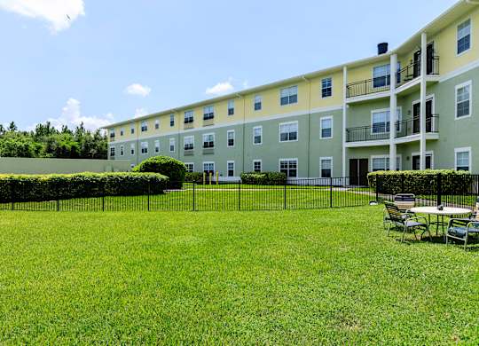 A grassy area in front of a building with a fence and chairs.