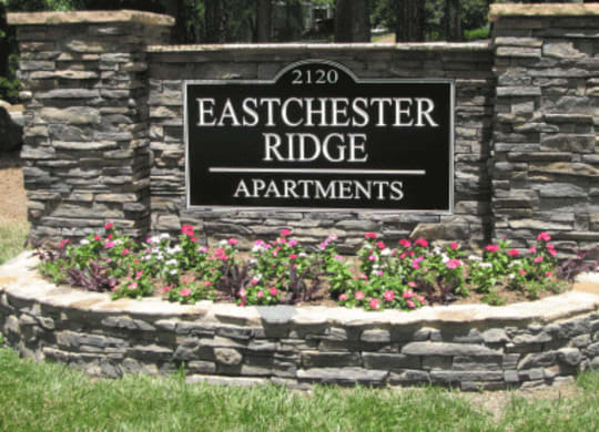 a stone retaining wall with flowers and a sign that says eastchester ridge apartments at Eastchester Ridge Apartments, High Point