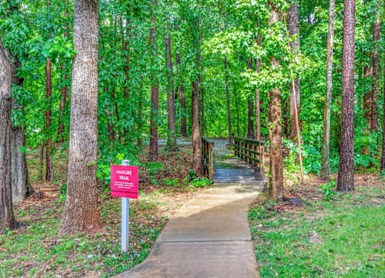a path through the woods with a red sign on the side of the path