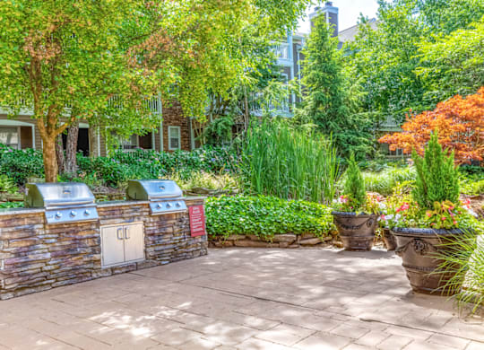 a brick patio with a barbecue and trees in the background