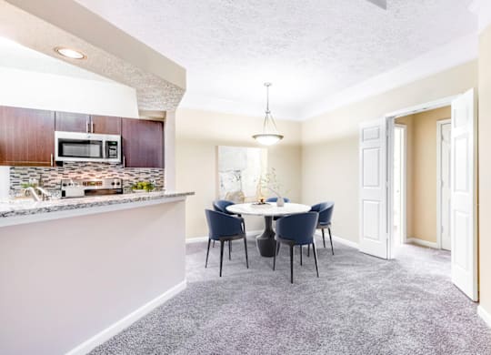 a dining area with a table and chairs and a kitchen in the background