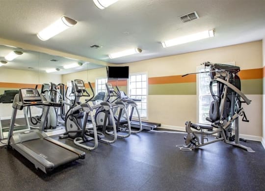 a gym with cardio equipment and large windows