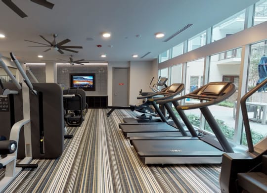 Interior of fitness center facing treadmills, workout equipment, and exterior windows