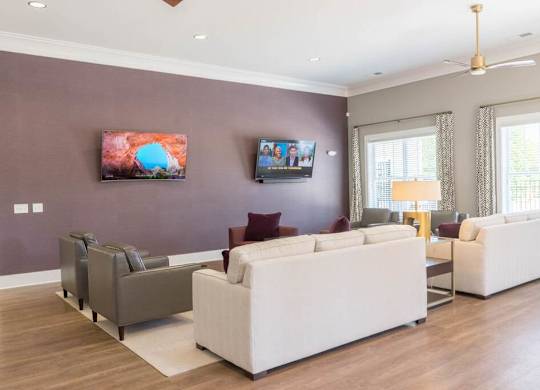 A living room with a white couch, grey armchairs, and a television on the wall at Foxwood Apartments, Raleigh-Durham, NC, 27616