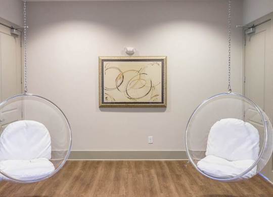 Two white chairs are suspended from the ceiling in a room with a framed artwork on the wall at Foxwood Apartments, North Carolina