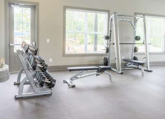 A gym with a row of dumbbells, a bench, and a weight machine at Foxwood Apartments, Raleigh-Durham, NC