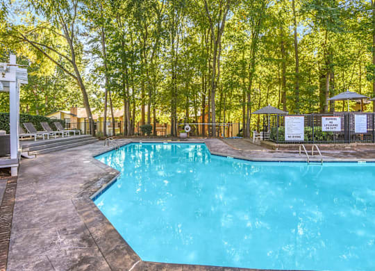 A pool surrounded by trees and a white pergola at Madison Southpark Apartment Homes, North Carolina, 28226