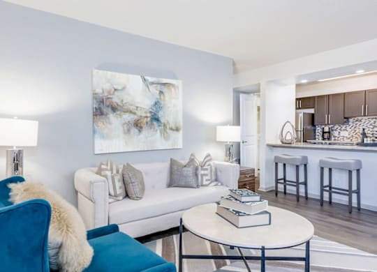 A blue chair with a white fur throw sits in a living room with a white couch and a large abstract painting on the wall at Madison Southpark Apartment Homes, North Carolina