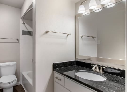 Bathroom with granite countertops, toilet, white shower tiles in shower with bathtub and towel bars.