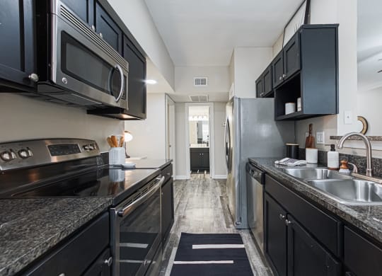 a kitchen with black cabinets, stainless steel appliances and granite-style countertops
