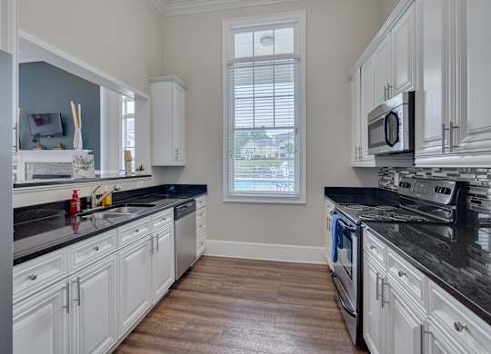 A kitchen with white cabinets and black countertops.