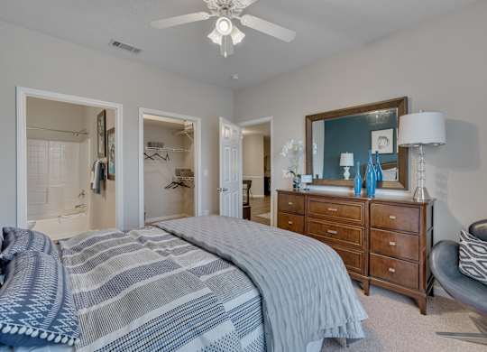 A bedroom with a bed, dresser, chair, and mirror.