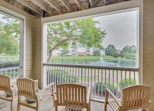 A balcony with four chairs and a view of a green lawn and trees.