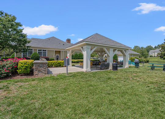 A gazebo is surrounded by a well-kept lawn and a stone wall.