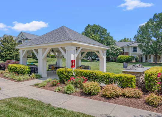 A gazebo is surrounded by bushes and flowers in a residential area.