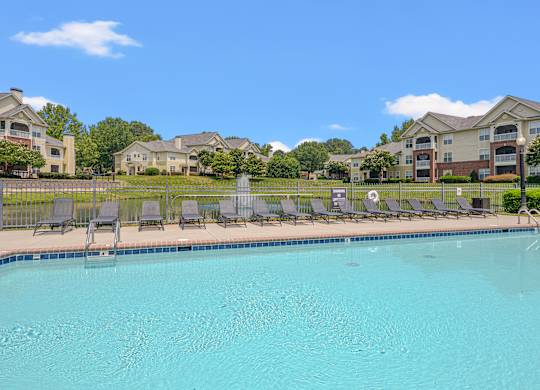 A swimming pool with lounge chairs and a row of houses in the background.