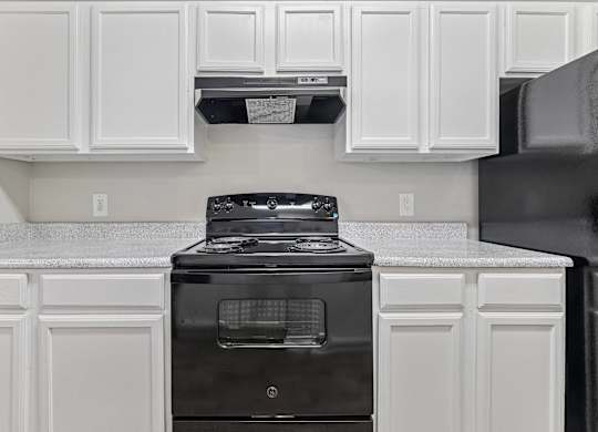 A black stove in a kitchen with white cabinets.