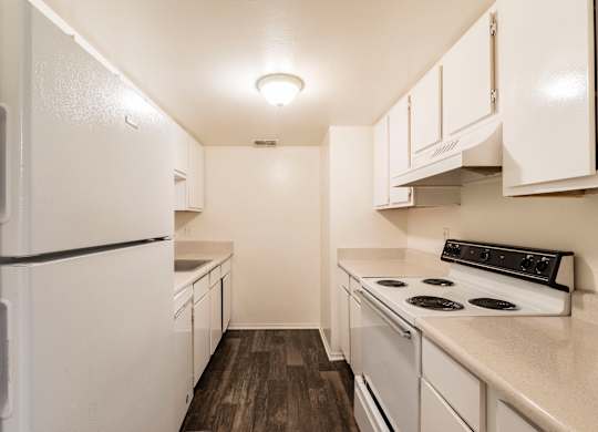 A white refrigerator is in a kitchen with a stove and cabinets.