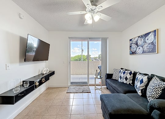 A living room with a flat screen TV mounted on the wall and a sliding glass door leading to a balcony.