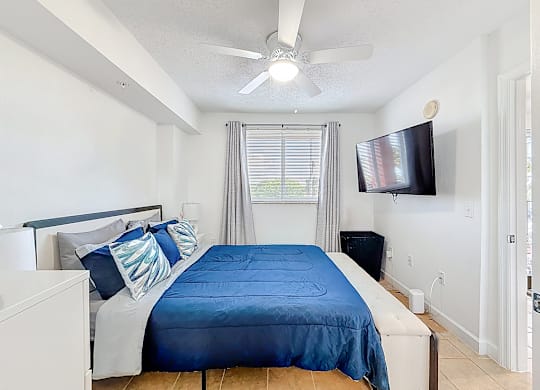 A bedroom with a blue bedspread and a flat screen TV mounted on the wall.